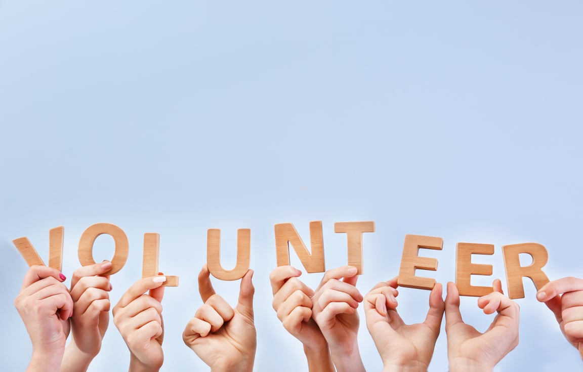 Raised Hands Holding Wooden Letters Forming the Word "Volunteer"